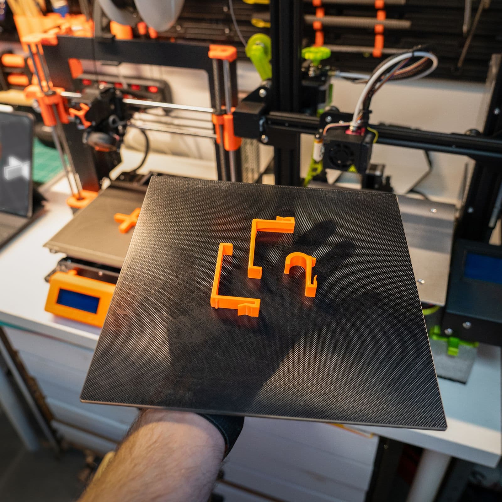 Piese portocalii printate 3D pe o placă de printare, ținută în mână în atelier