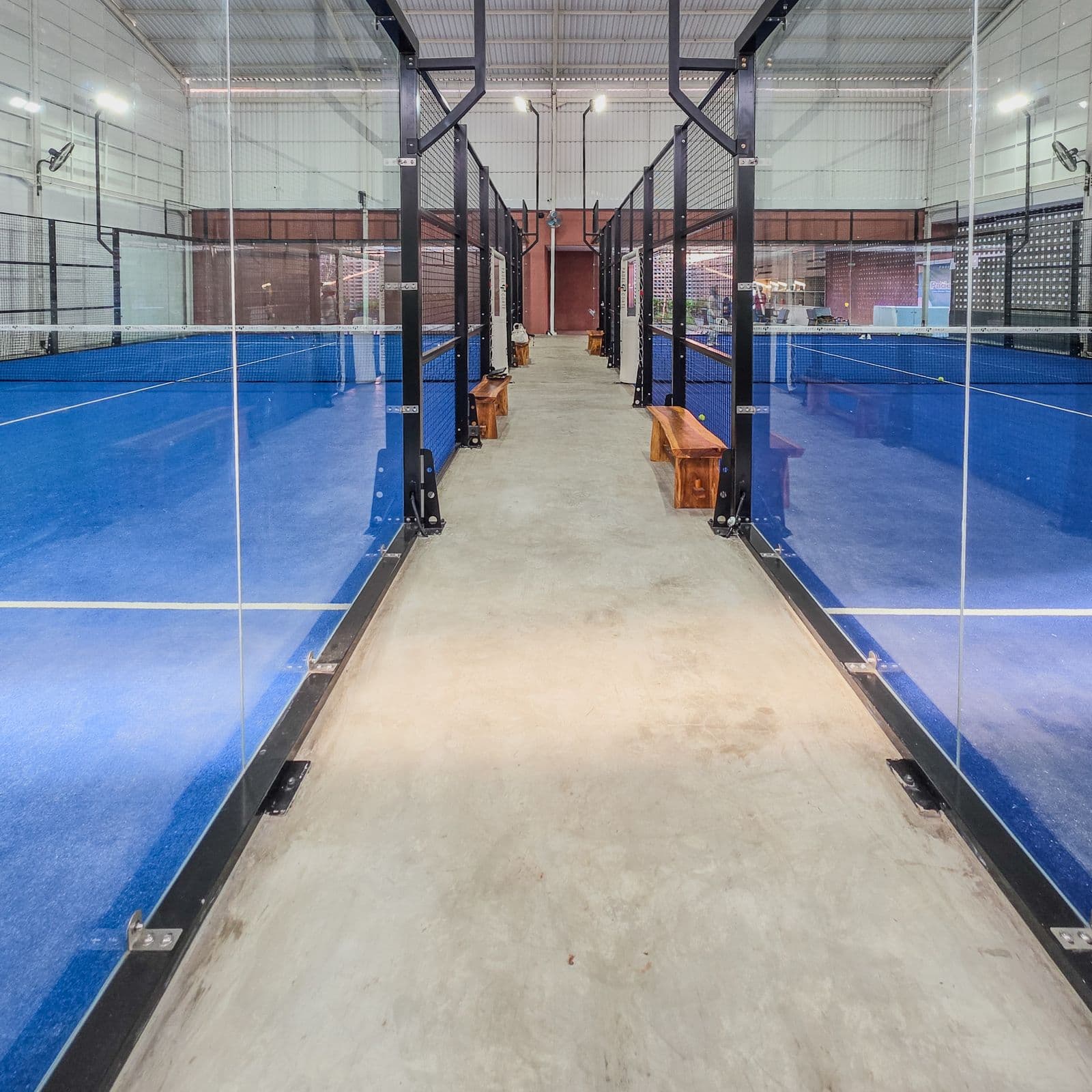 Două terenuri de padel cu suprafață albastră, pereți de sticlă și stâlpii de oțel pe care se prind suporturile